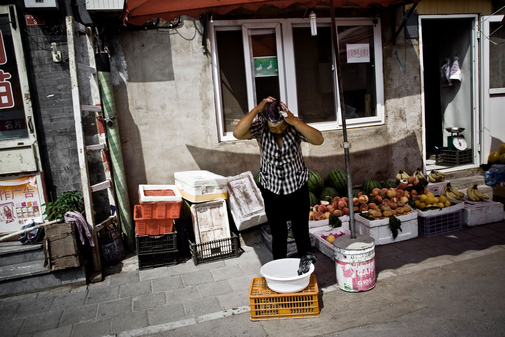 CHINA. Beijing, September 2012. A vegetables seller washes her hairs.